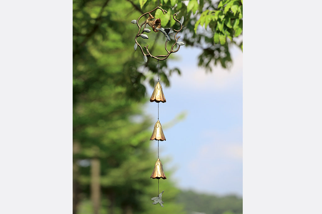 sculpted metal wind art with motif of encircled lily and hummingbird with 3 lily blossoms suspended below with a hummingbird pendant
