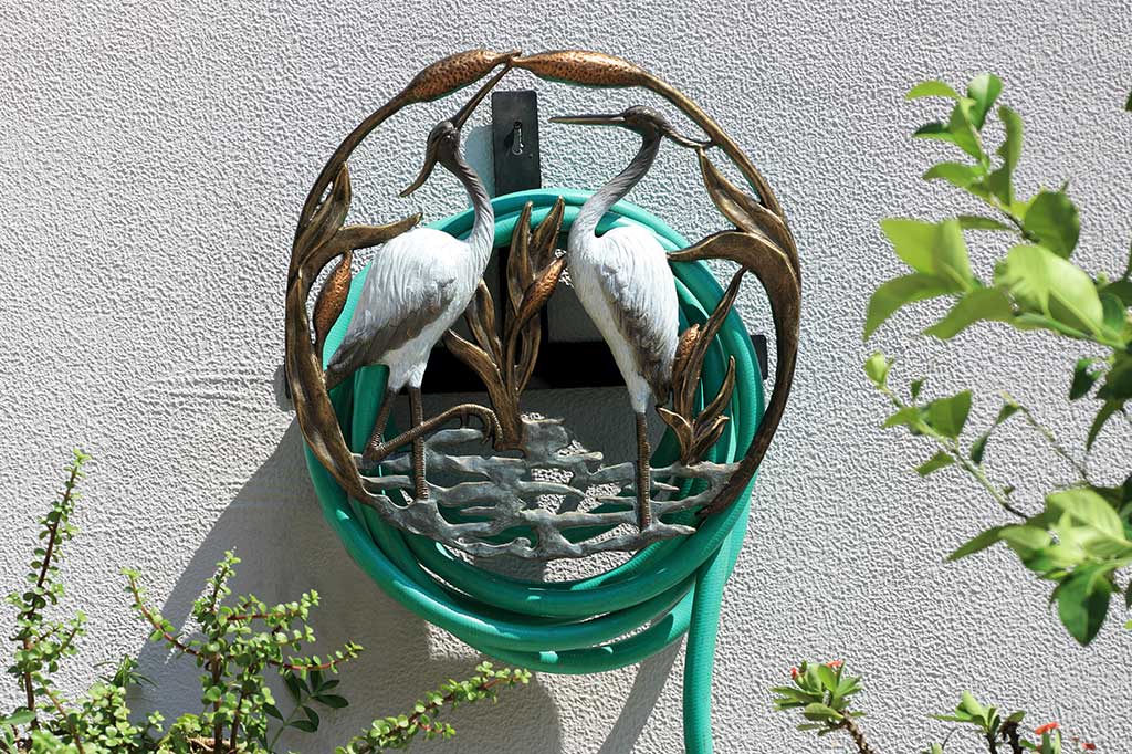 hose holder on stucco wall with hose; motif of two white herons standing in cattail reeds