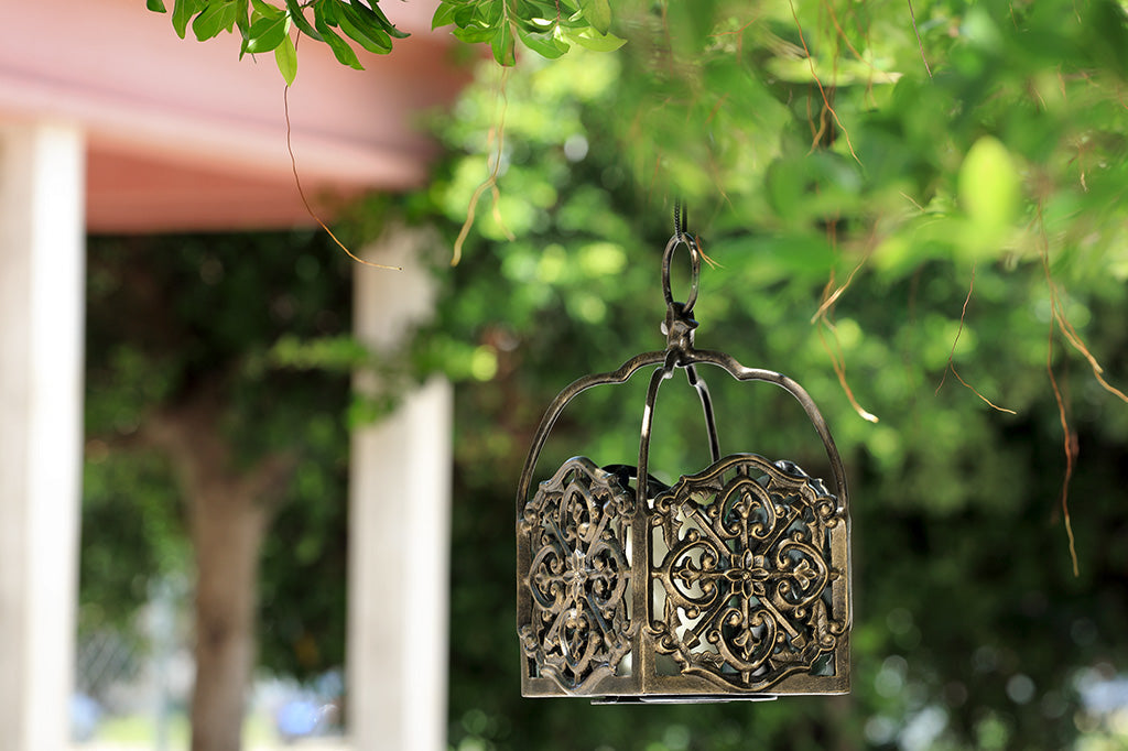 italianate fretwork hanging lantern box with 1 pillar candle shown in garden near tree