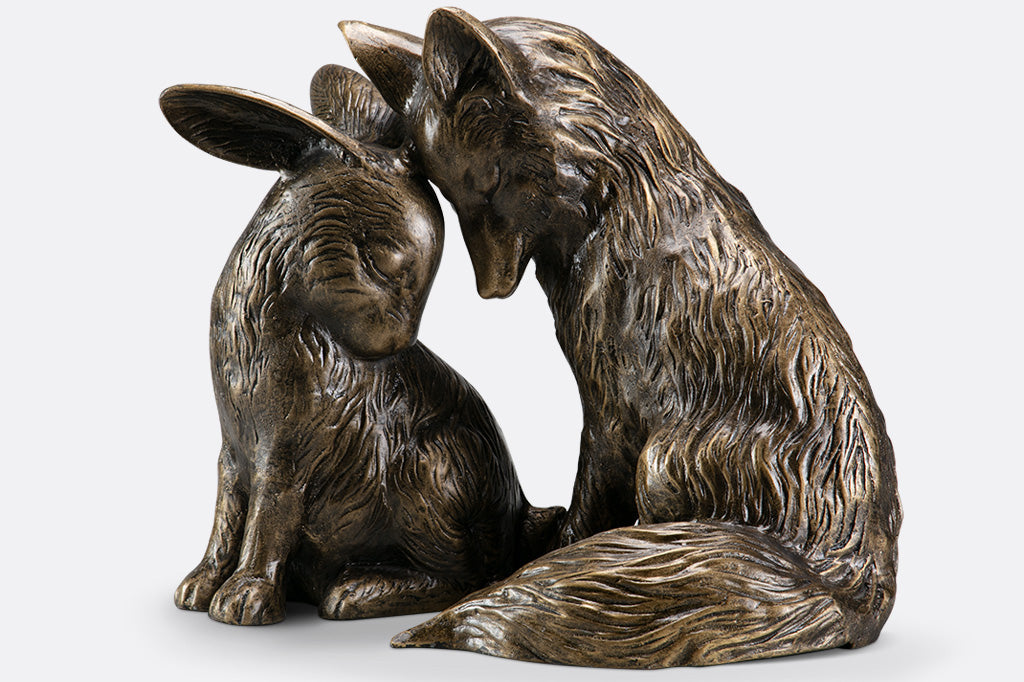 side view of garden sculpture of fox and rabbit tenderly nuzzling