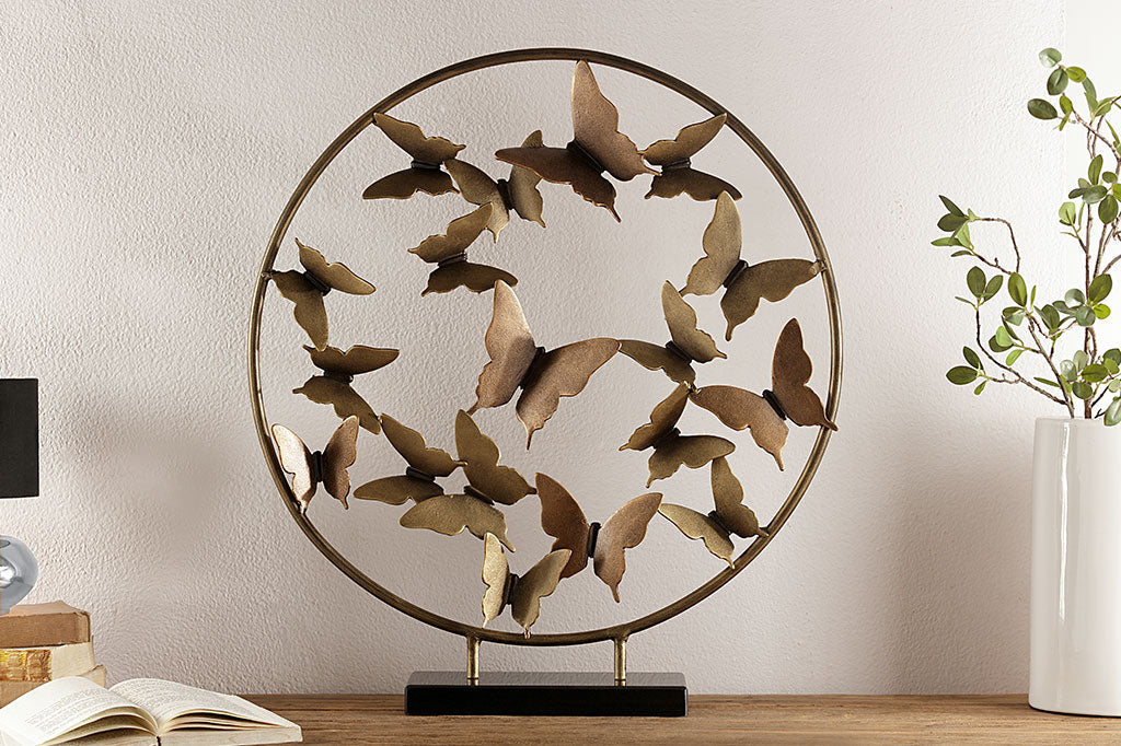 Brass Butterfly burst with marble base shows sculpture of hoop filled with butterflies placed upon desk near books and vase of branches