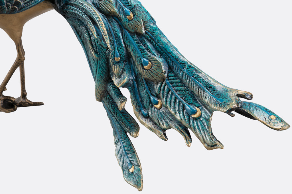 cast metal peacock with blue feathers standing proudly