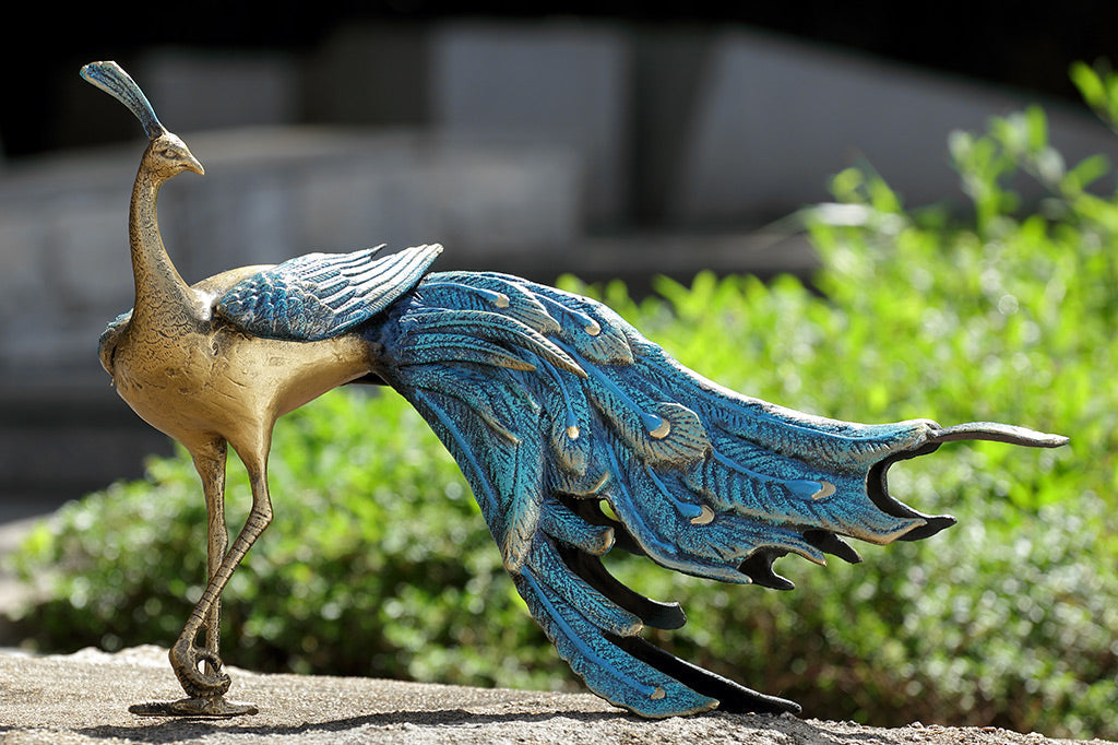 cast metal peacock with blue feathers standing proudly by garden bed