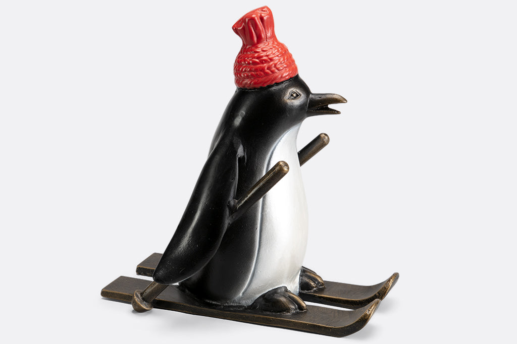 cast metal skiing penguin sculpture wearing a red knit hat