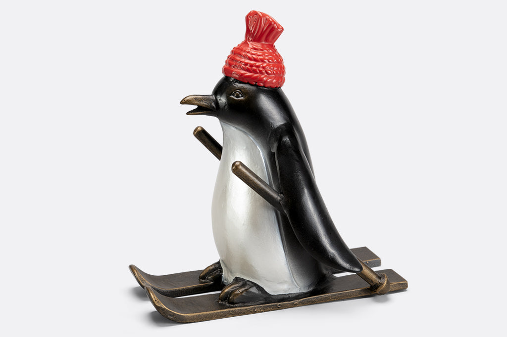 cast metal skiing penguin sculpture wearing a red knit hat