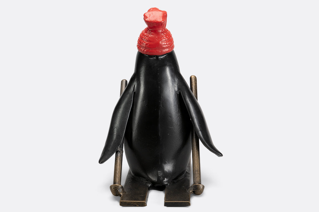 cast metal skiing penguin sculpture wearing a red knit hat