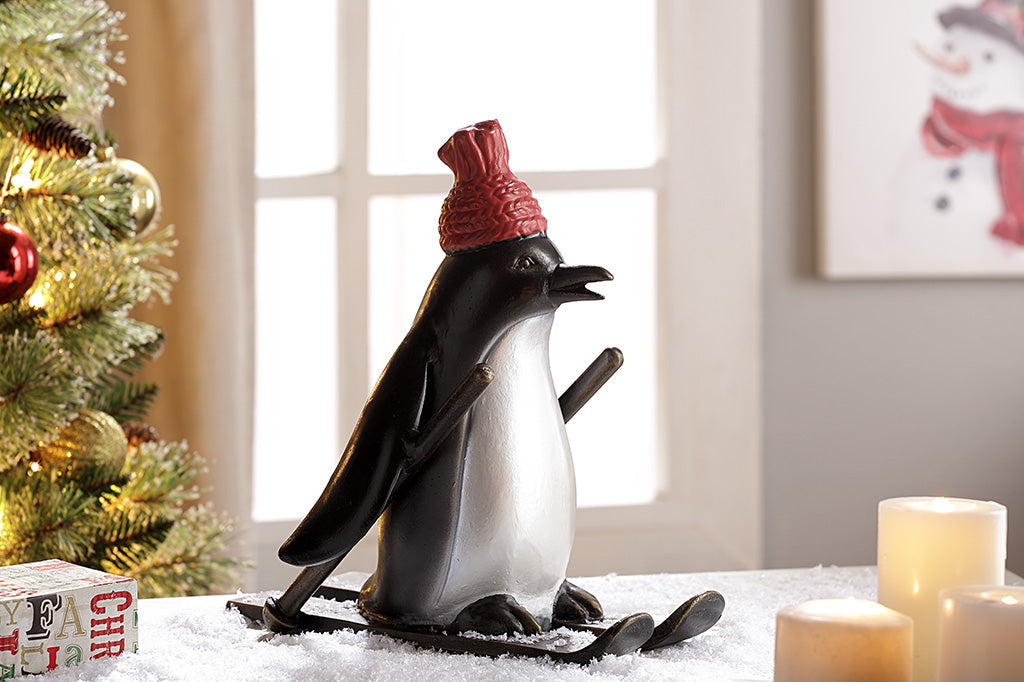 cast metal skiing penguin sculpture wearing a red knit hat set in holiday scene