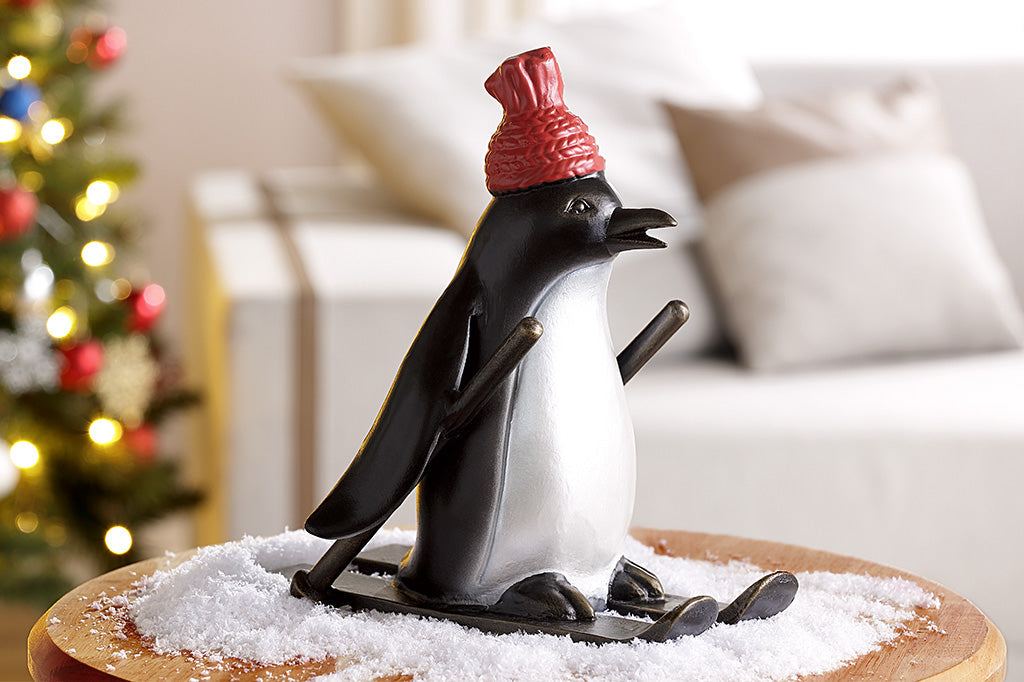 cast metal skiing penguin sculpture wearing a red knit hat