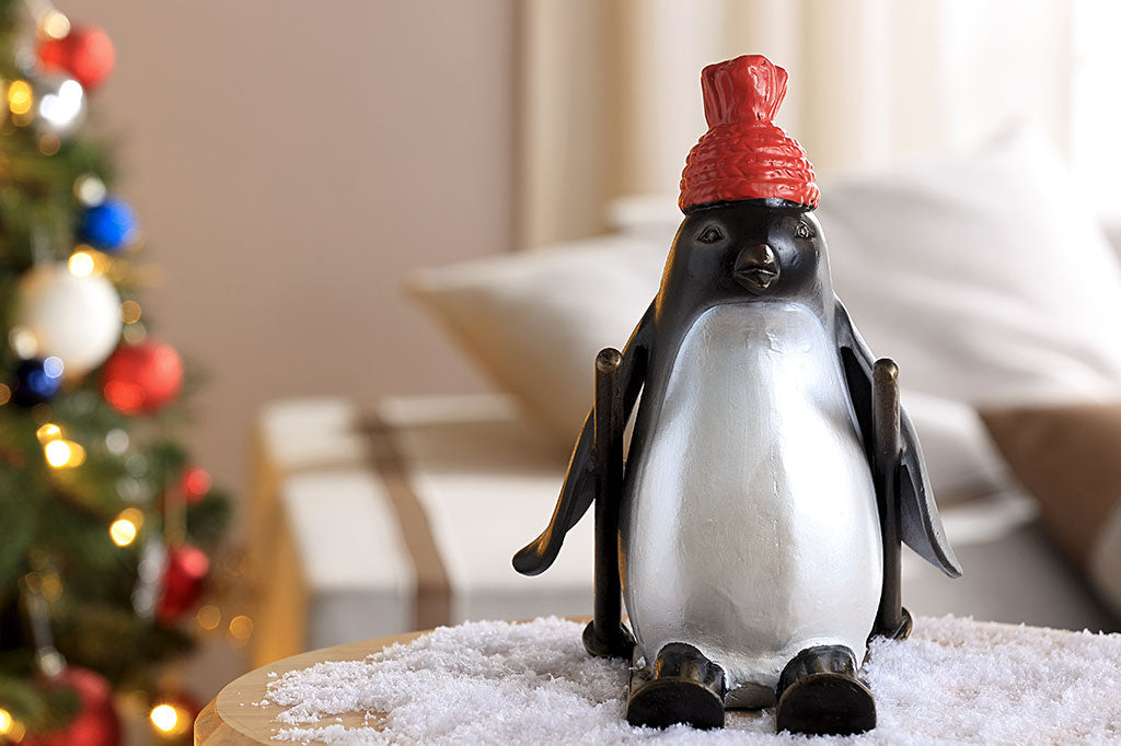 cast metal skiing penguin sculpture wearing a red knit hat