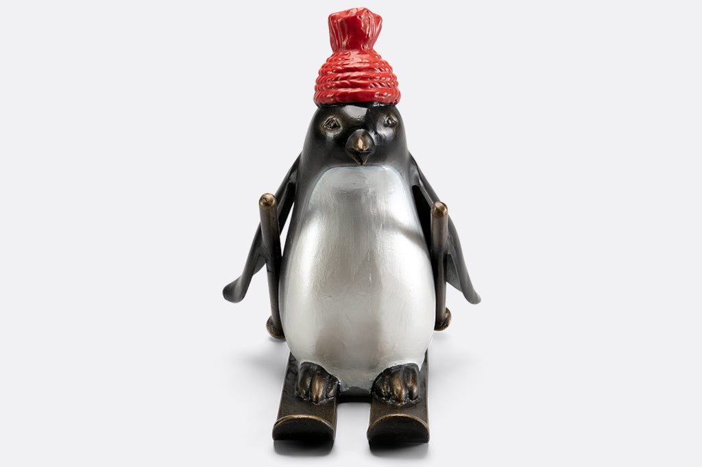cast metal skiing penguin sculpture wearing a red knit hat