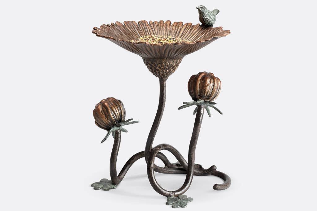 Clover and blossom shaped bird feeder has sculpted bird perched on rim. Feeder holds birdseed