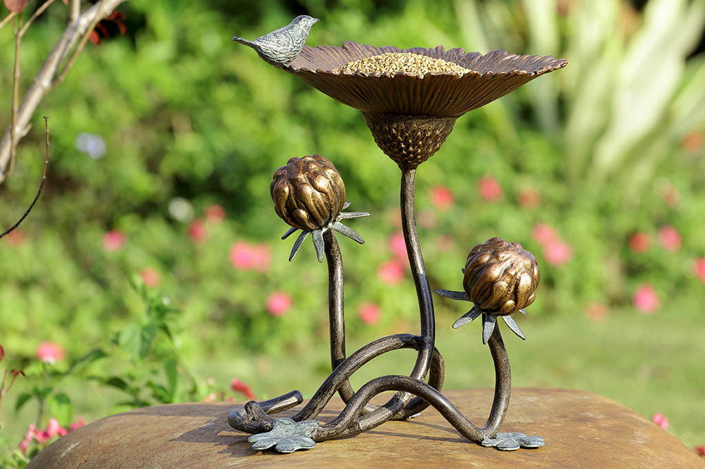 Clover and blossom shaped bird feeder has sculpted bird perched on rim, shown on rock in garden