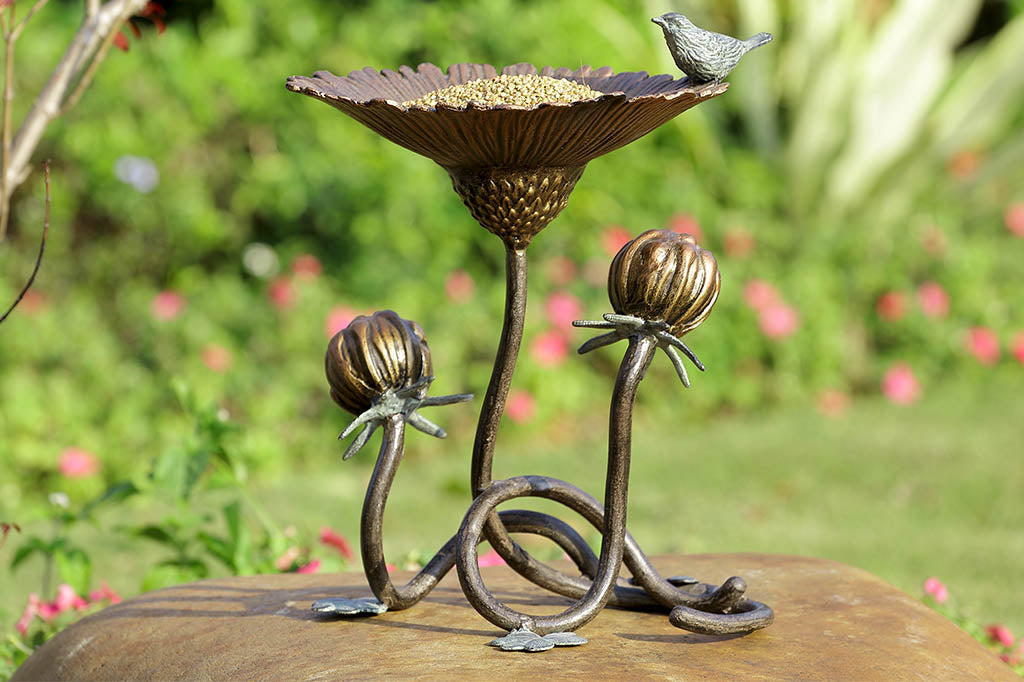 Clover and blossom shaped bird feeder has sculpted bird perched on rim, shown on rock in garden