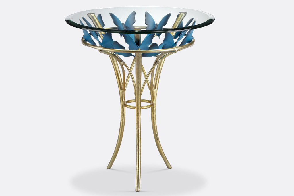 modern table with gold finish table supports and blue butterflies; glass top with beveled edge, side view
