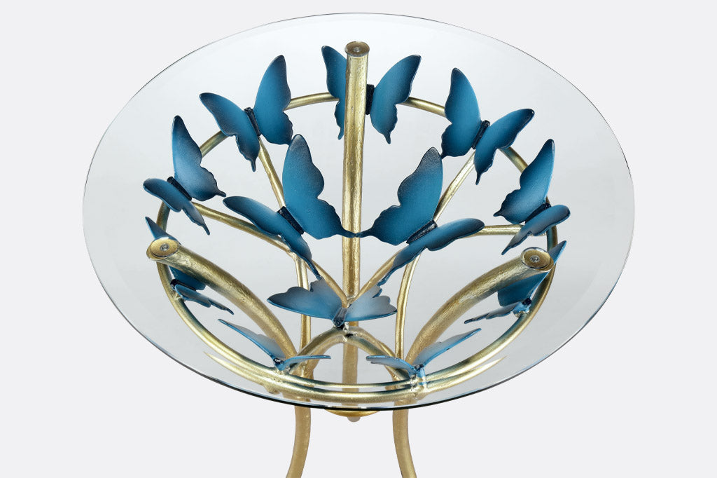 Top View of modern table with gold finish table supports and blue butterflies; glass top with beveled edge