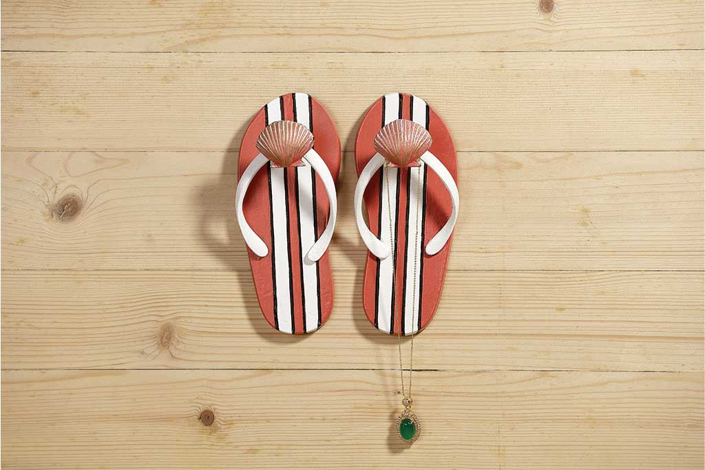 Pair of wall hooks shaped like flipflops holding a necklace on a wood wall #color_melon