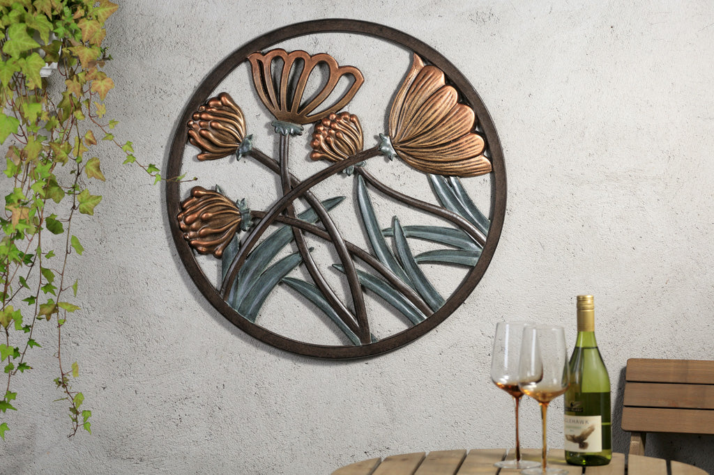 Cast metal circular wall plaque of thistle and blossom is displayed on a wall by a cafe table with wineglasses