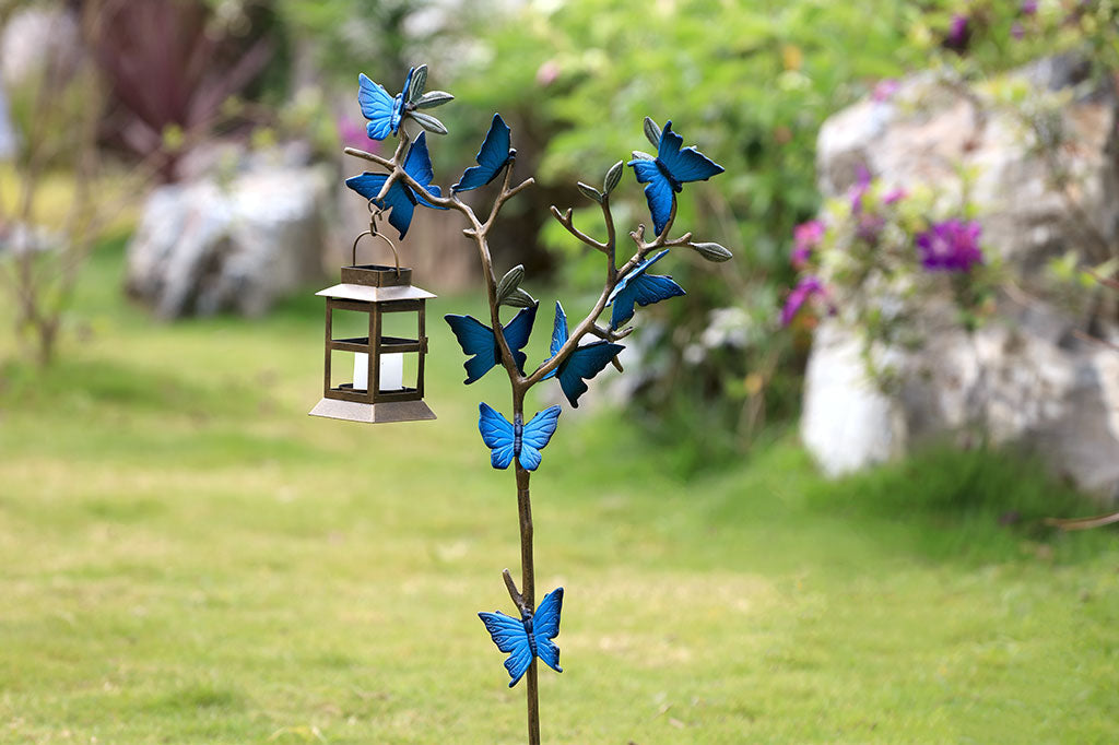 Staked Garden Lantern shown in garden; design is branch covered with blue butterflies and holds iron little lantern holding tea light
