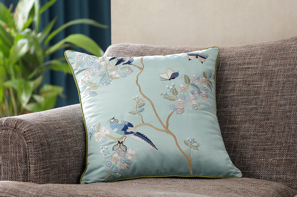 light blue satin pillow with embroidered details placed on couch  