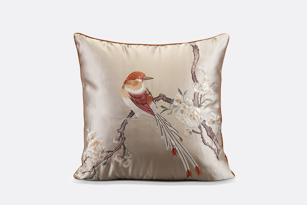 gold colored satin pillow with embroidered imagery of bird perched on flowering branch