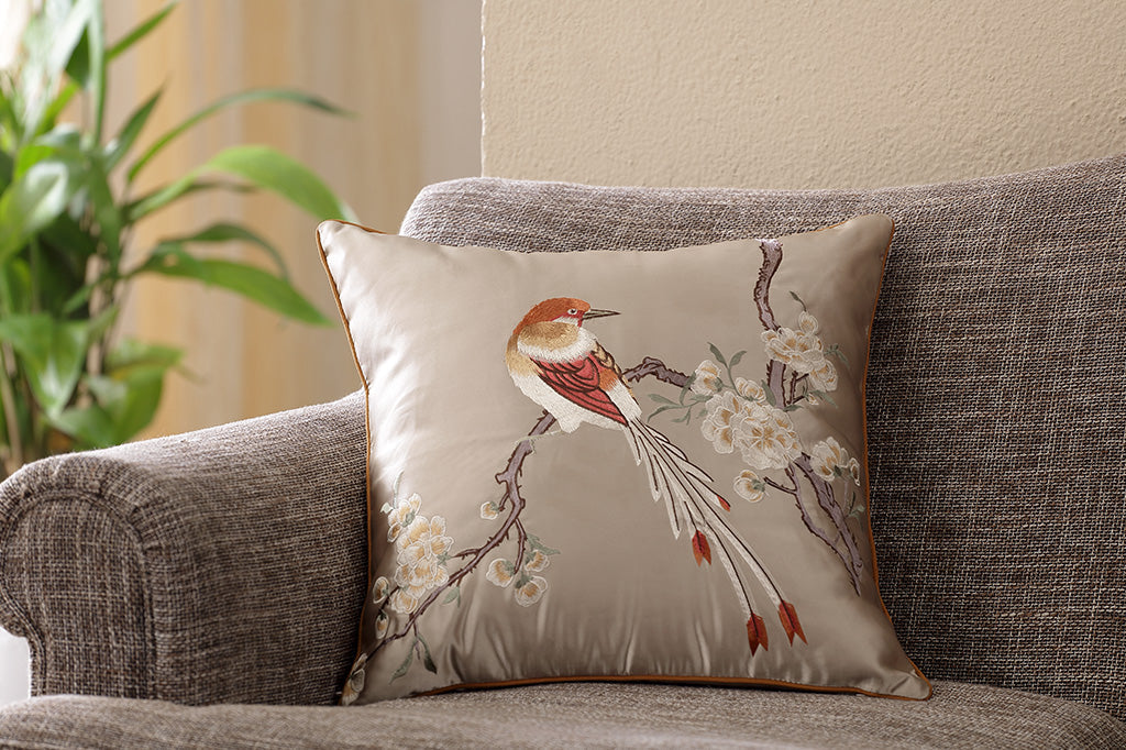 satin gold pillow with embriodered imagery of bird perched on flowering branch set on couch 