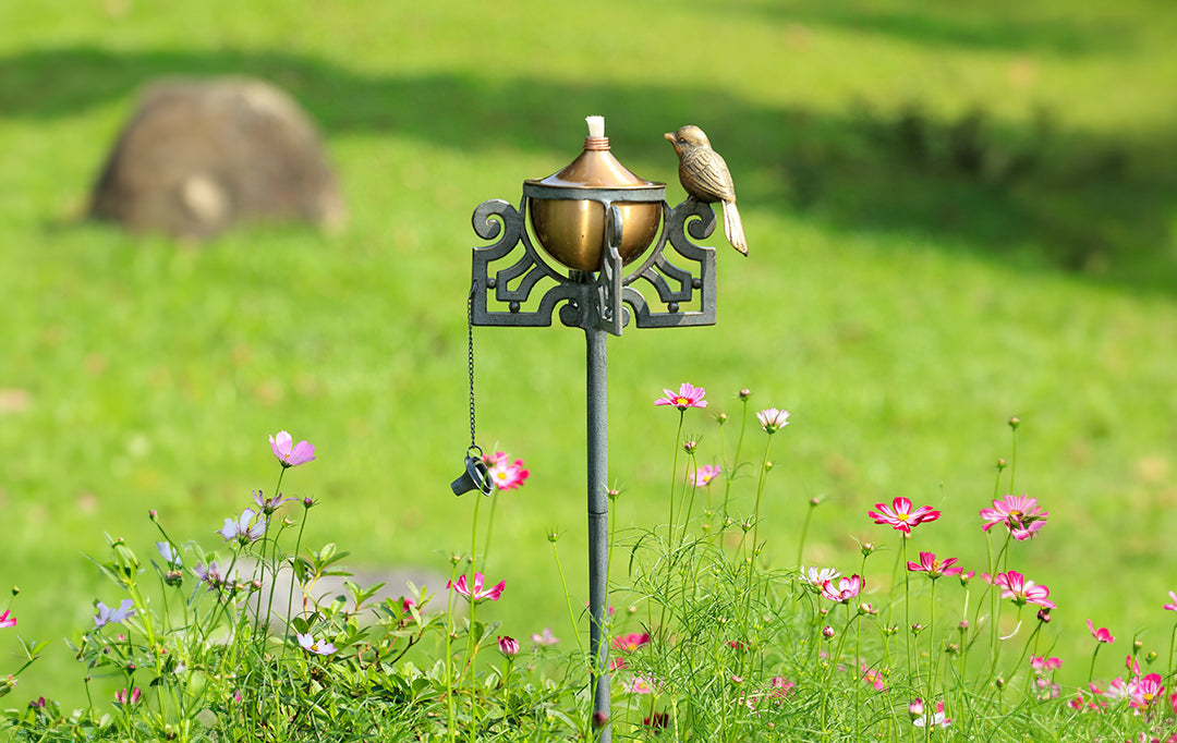 Mission style motif of scrollwork and bird on a garden oil torch shown amidst flowers