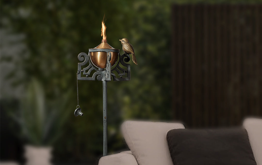 Mission style motif of scrollwork and bird on a garden oil torch shown at dusk with lit oil wick placed in a patio