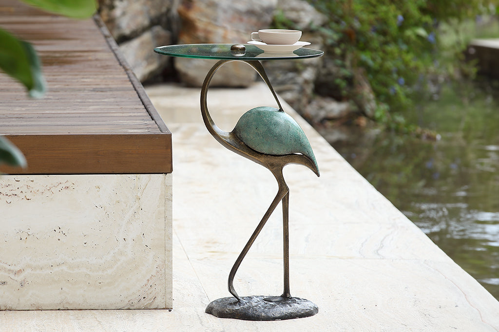 Elegant crane sculpture is the base for a drink table with glass top - shown in garden with teacup, by a reflecting pool