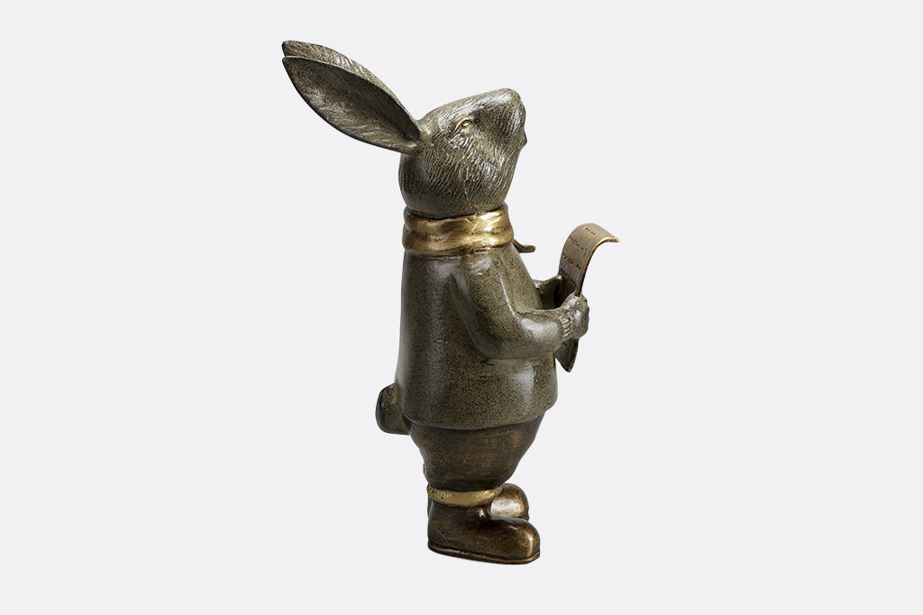 Caroling bunny sculpture holding a music sheer and wearing a hold scarf side view facing right