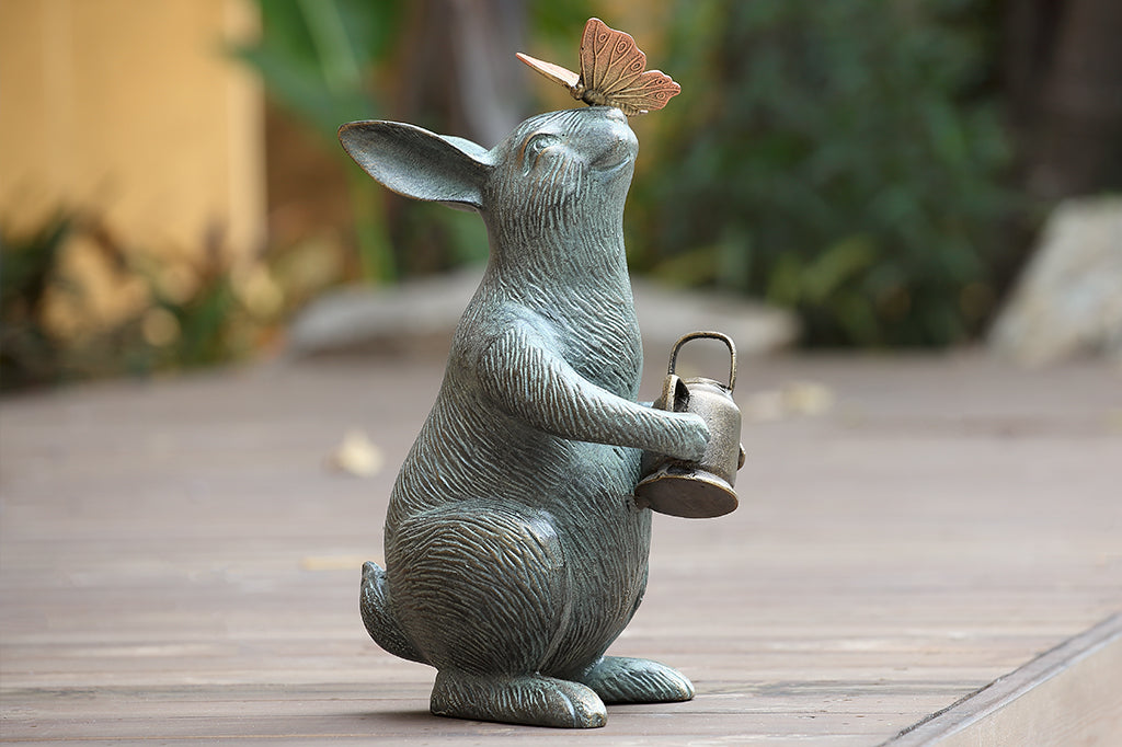 Garden sculpture of bunny holding watering can and looking at butterfly perched on its nose