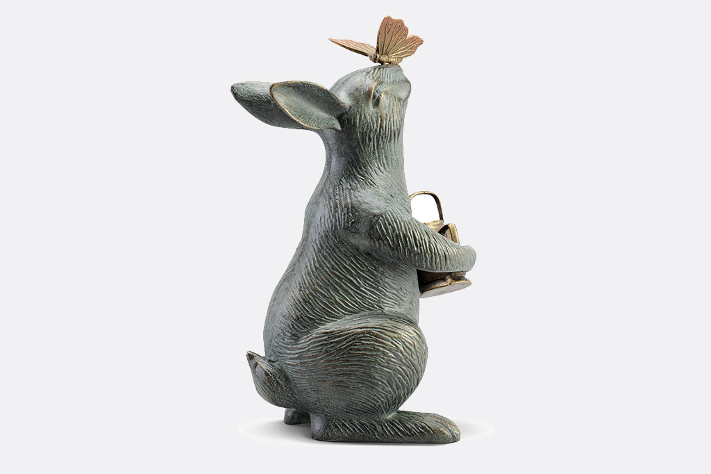 back view of Garden sculpture of bunny holding watering can and looking at butterfly perched on its nose