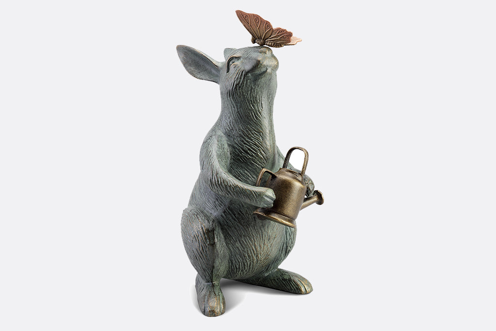 Garden sculpture of bunny holding watering can and looking at butterfly perched on its nose
