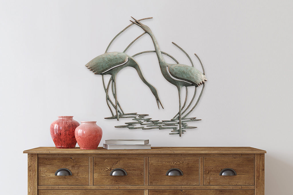 Wall plaque of two cranes standing in reeds and water - above a dresser with ceramic vases