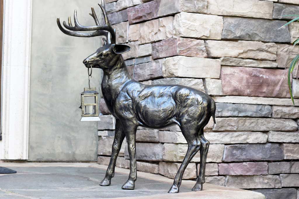 cast metal deer sculpture holding lantern in mouth set on front porch
