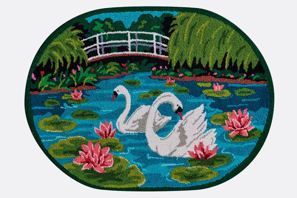 rounded rectangle hooked wool rug, depicting a pond scene with swans, lilies and bridge in background
