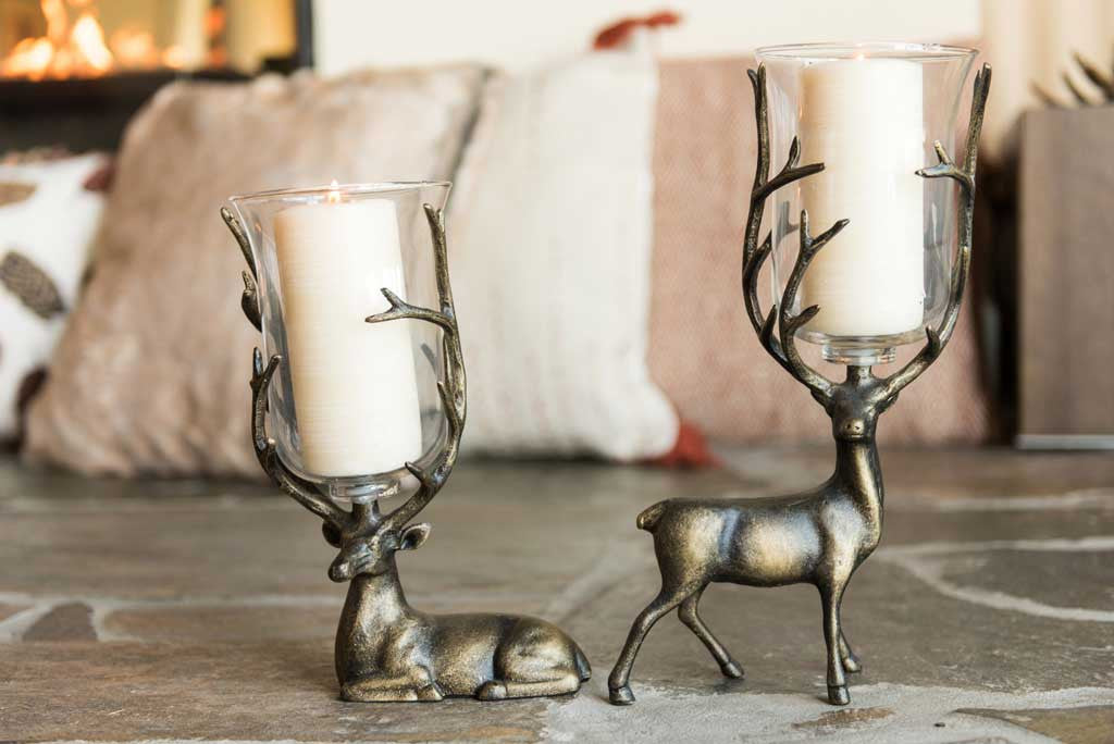 Two sculpted deer, one seated, hold a pillar candle in glass between antlers