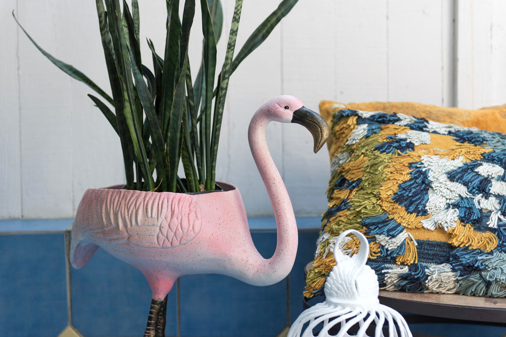 Festive Flamingo Planter & Beverage Tub shown being used as plantholder in a tiled patio area. pillows in background