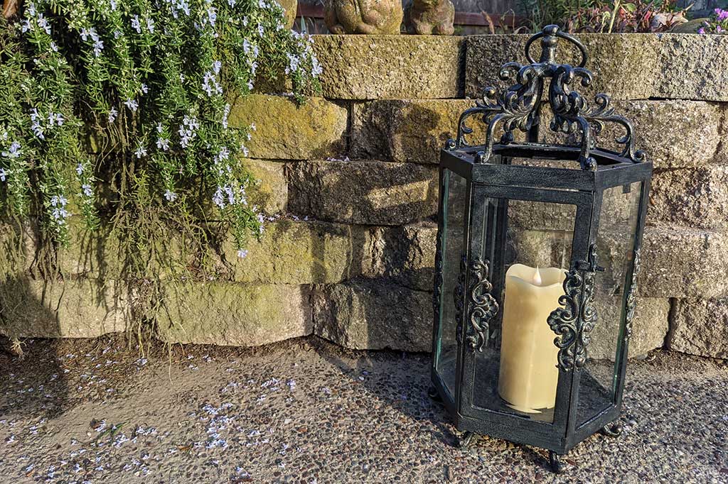 Rouleau Six Pane Lantern in a garden setting, by retaining wall and hanging rosemary