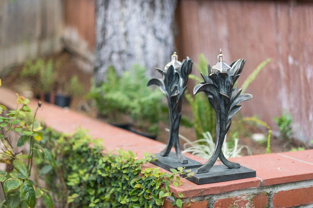 Outdoor oil torch in style of plant, sculpted zinc and verdigris colors on metal, 2 shown on brick wall in garden