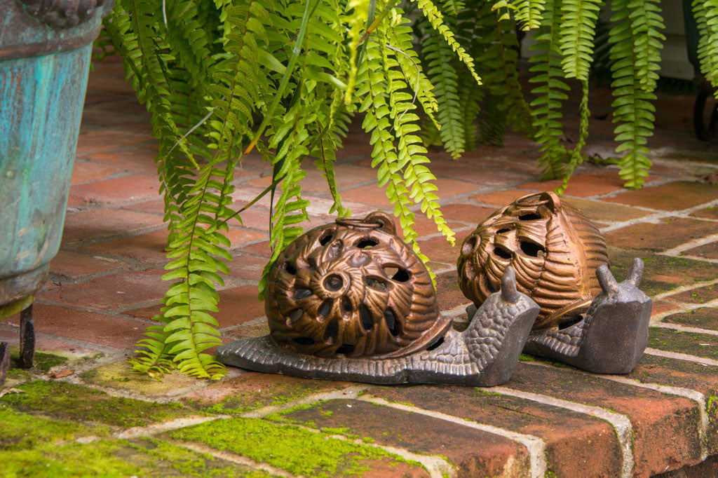 2 Garden Snail Lanterns shown on outdoor, mossy brick steps under hanging ferns