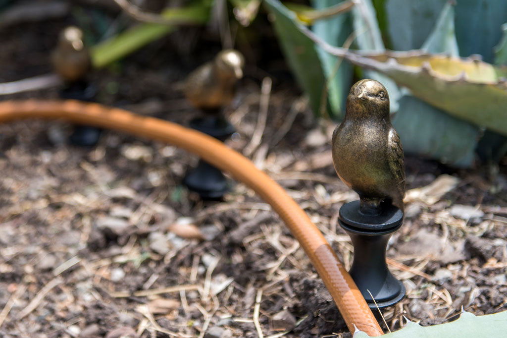 Proud Bird Hose Guard shows perky bronze bird on stake designed to keep the hose from hitting ground plants