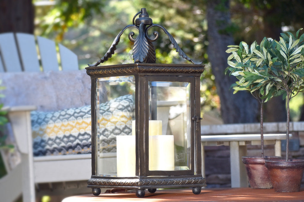 Foglia lantern features acanthus leaf corner accent, shown with cream candles in a backyard villa setting