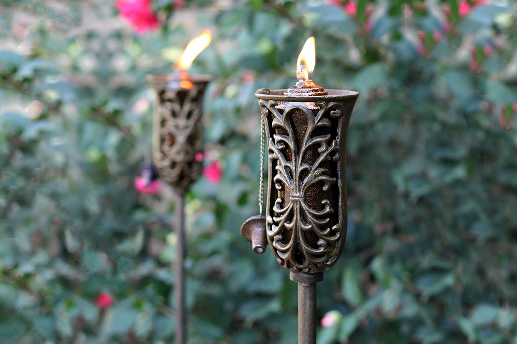 scrollwork adorns oil torch in front of rose hedge