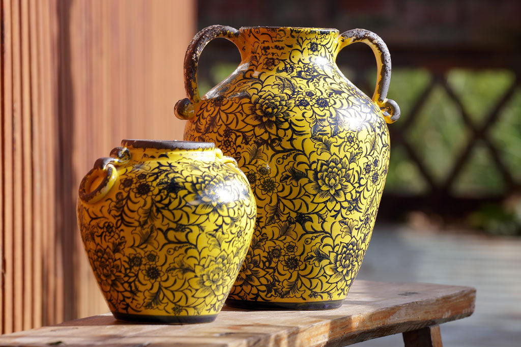 Pera Pot and Giallo Vase have matching floral and vine motif. Pictured together on a bench in the sun.