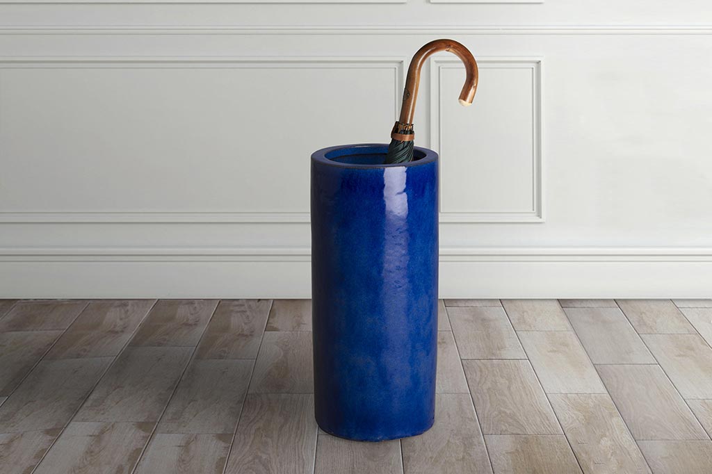 ceramic tall blue cylindrical umbrella stand shown in home interior holding umbrella