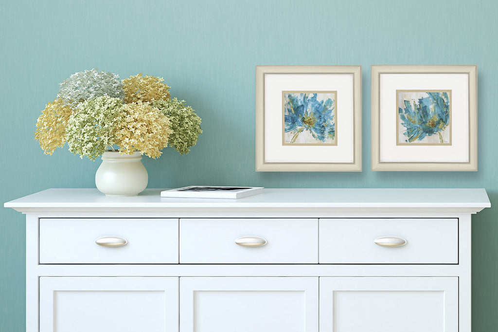 pair of framed blue impressionist style flowers in square format hung above a white dresser in blue room
