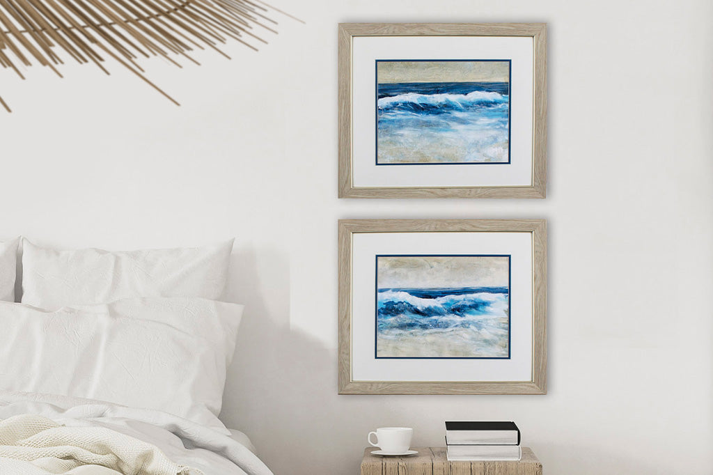Two wave paintings inside a wooden frame on white wall besides bed