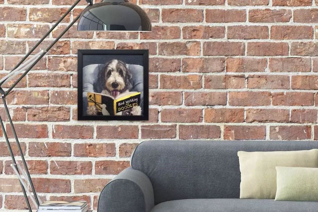framed art print of dog reading in bed a book about bird watching, shown on brick wall above a couch