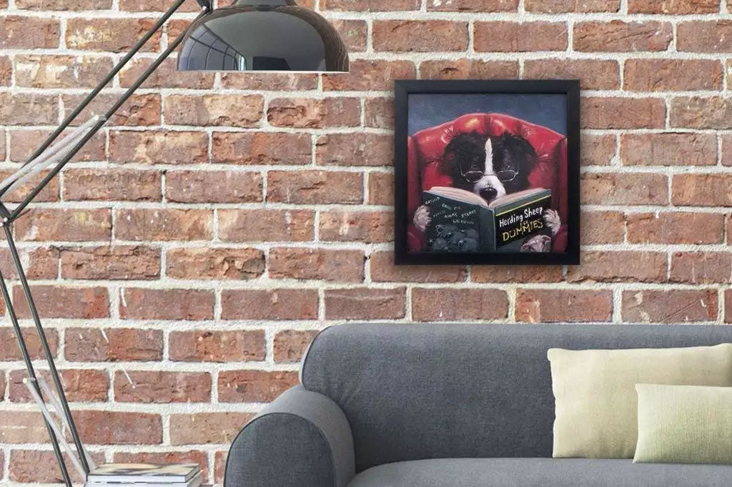 textured dog reading a book wearing glasses seated in red plush arm chair framed painting. on brick wall above couch