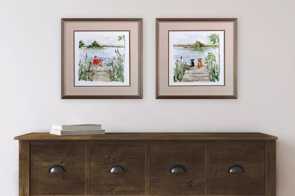 two framed art pieces on wall, boy and dog fishing on dock and two dogs sitting on sock over looking lake